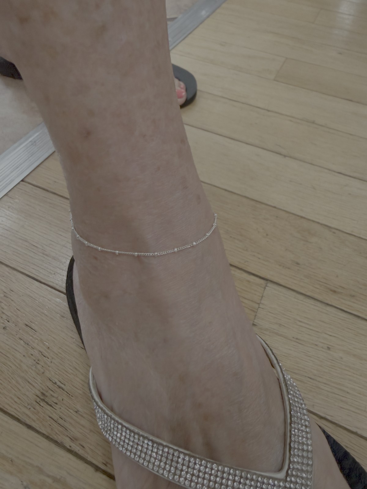 A delicate single chain anklet above a sandal