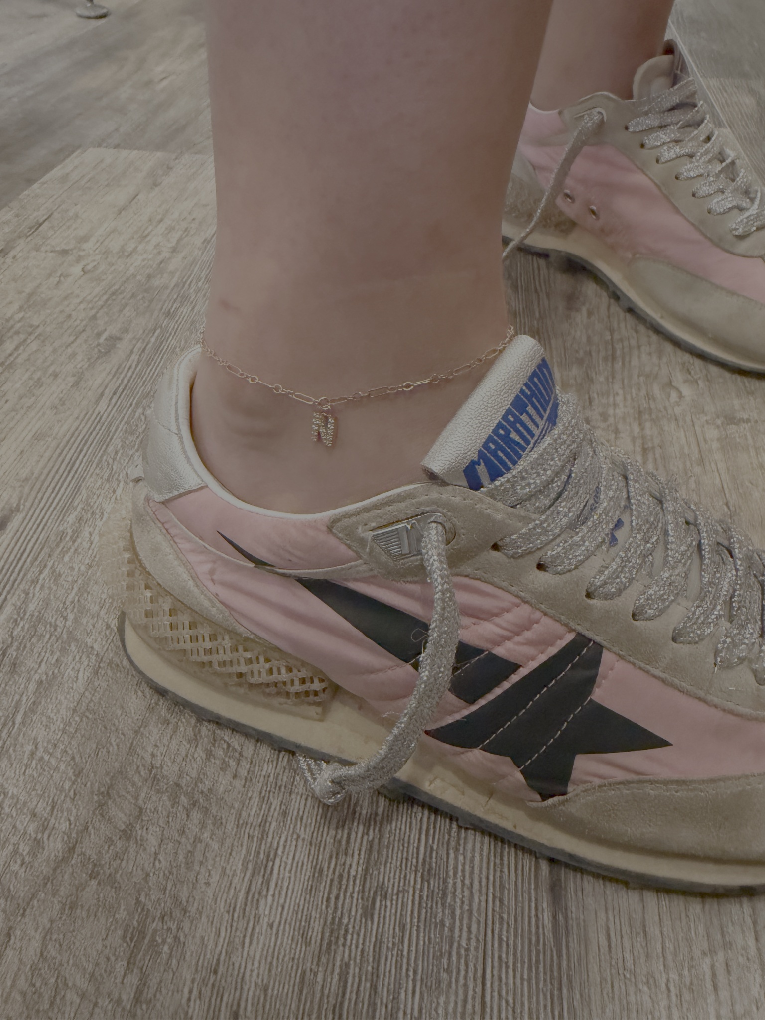A fine chain anklet with a sparkling dangling charm above a pink sneaker