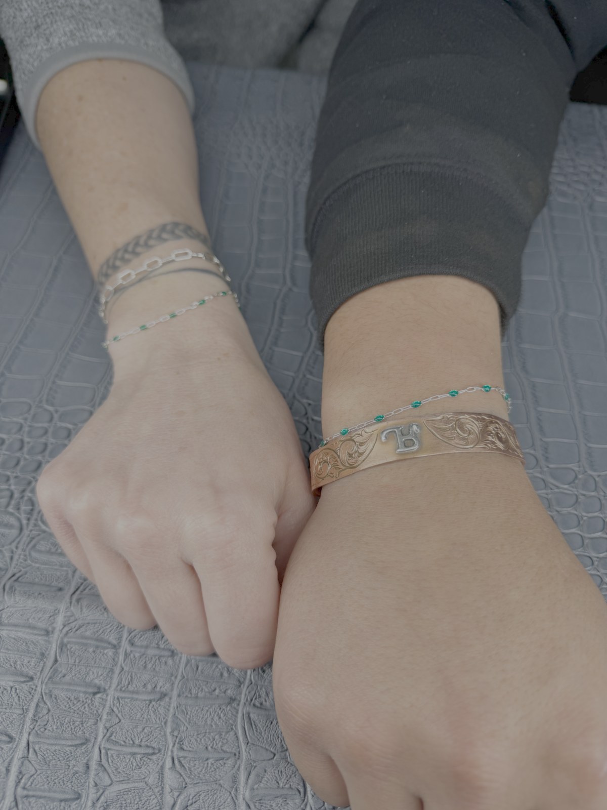 Two wrists showing gold chains and colorful bracelet layers