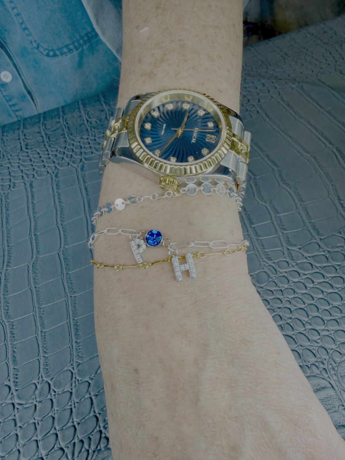 A gold bracelet stack with personalized charms beside a watch