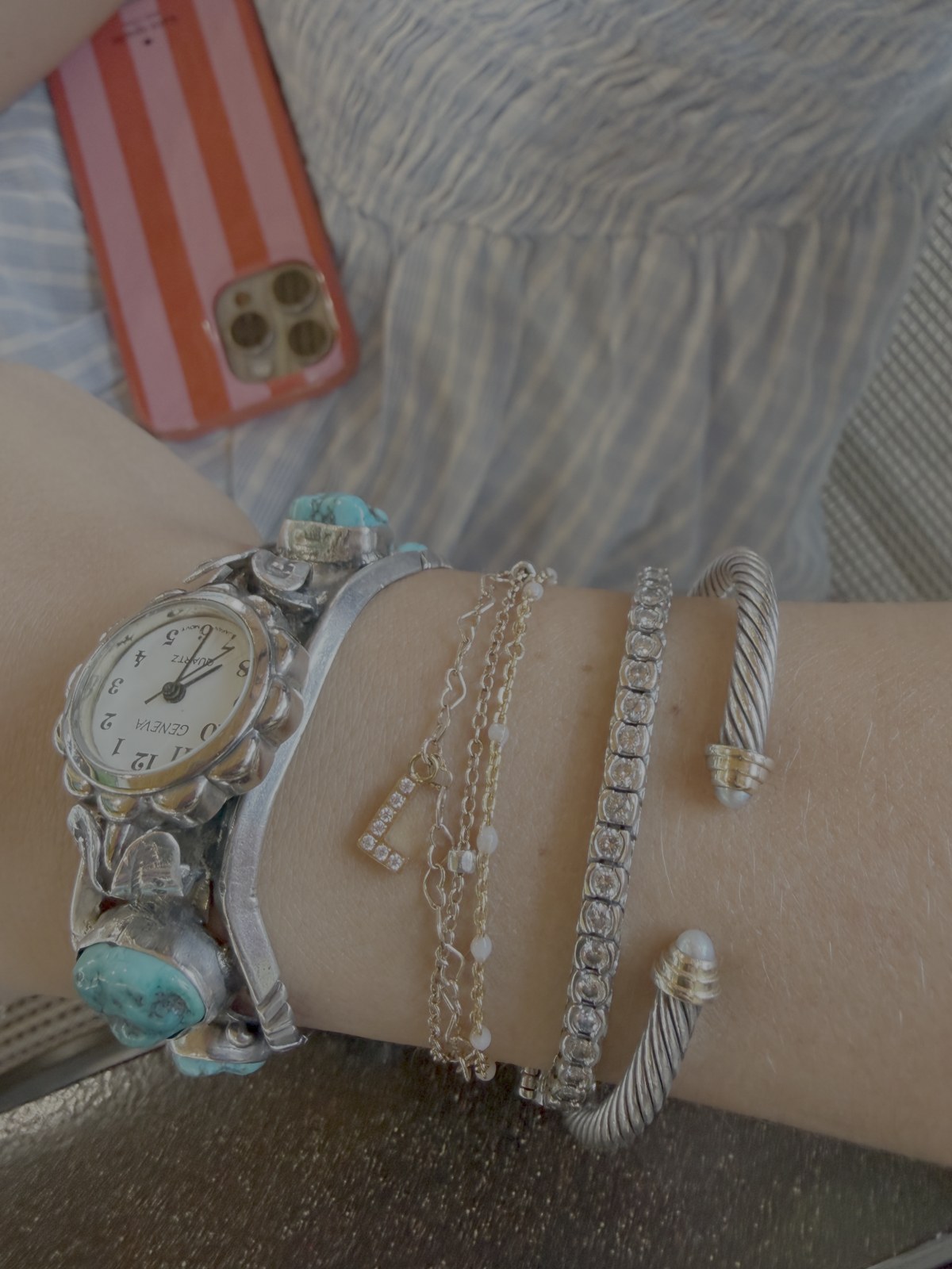 Gold chain bracelets layered alongside a watch and cuff